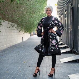 Stylish woman wearing a floral abaya and hijab, confidently posing outdoors.